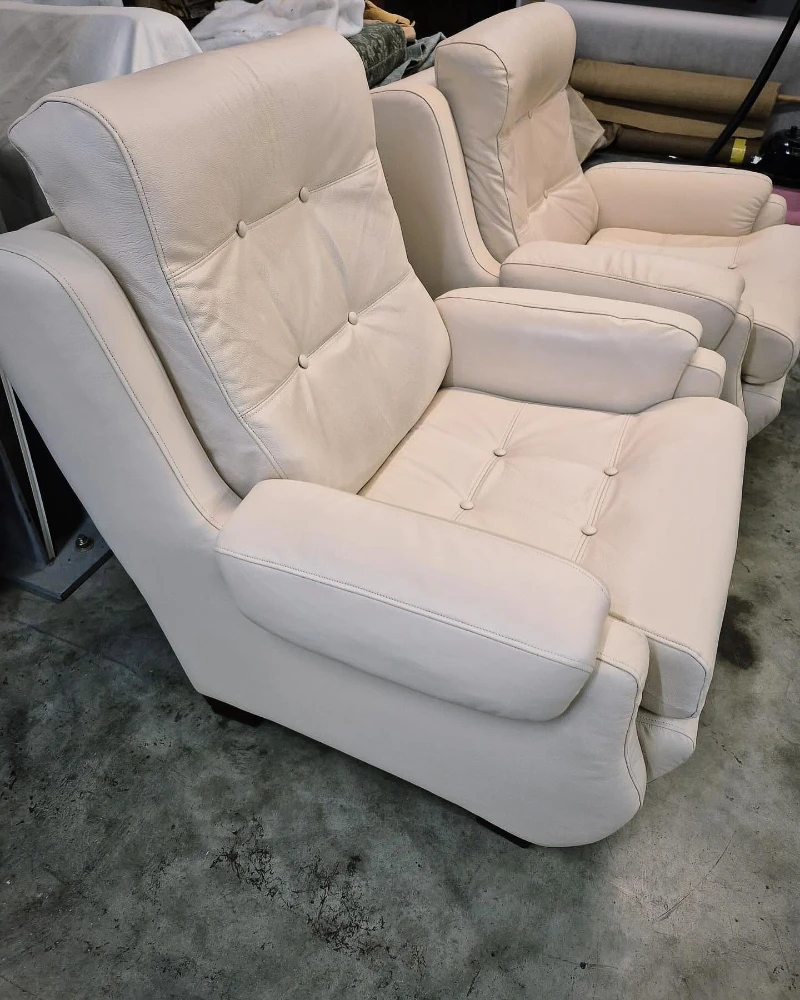 Two cream leather armchairs with padded arms and buttoned seat and back cushions.