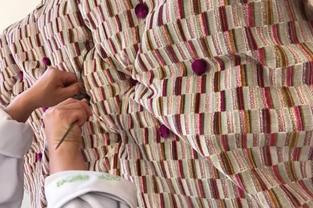 Upholsterer hand-tufting a striped bespoke headboard with purple buttons.