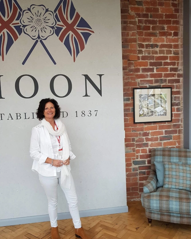 Woman standing beside a blue tartan armchair in an interior furnishings showroom with exposed brick walls.