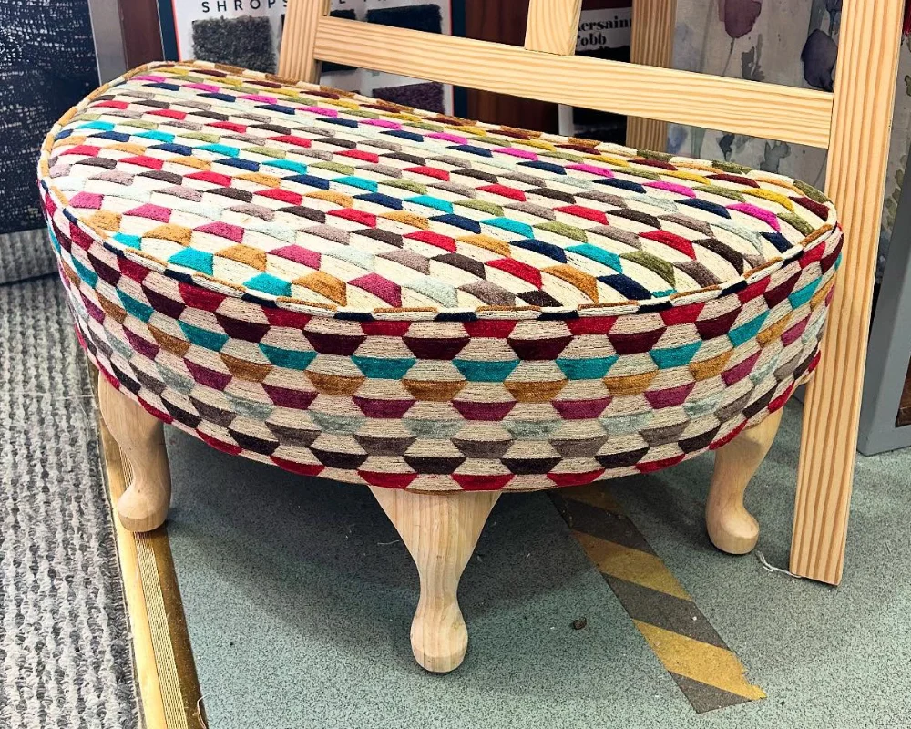 Oval footstool upholstered in multicoloured geometric fabric with natural wooden legs.